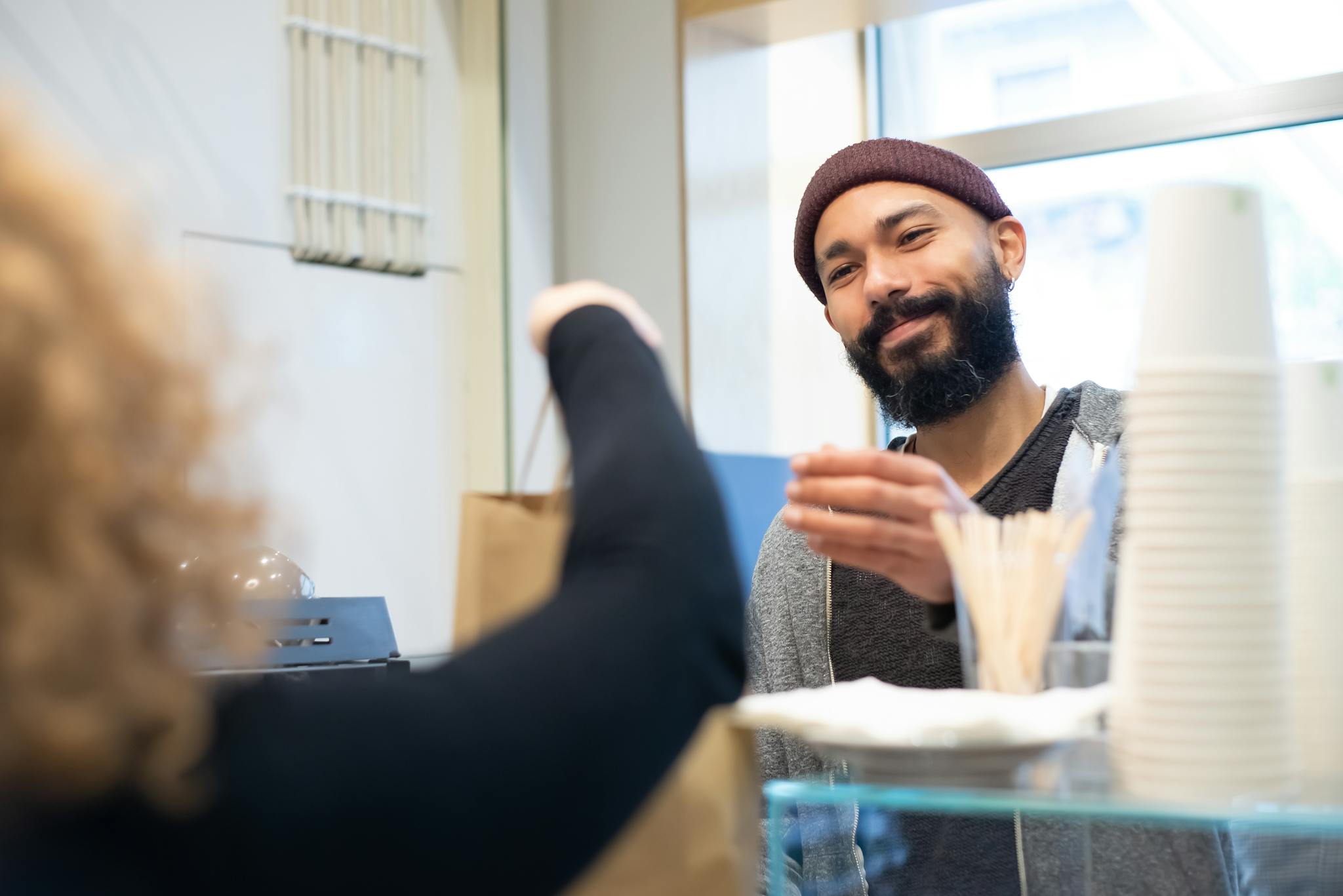A smiling barista hands over a paper bag to a customer in a cozy café, showcasing warm customer service.