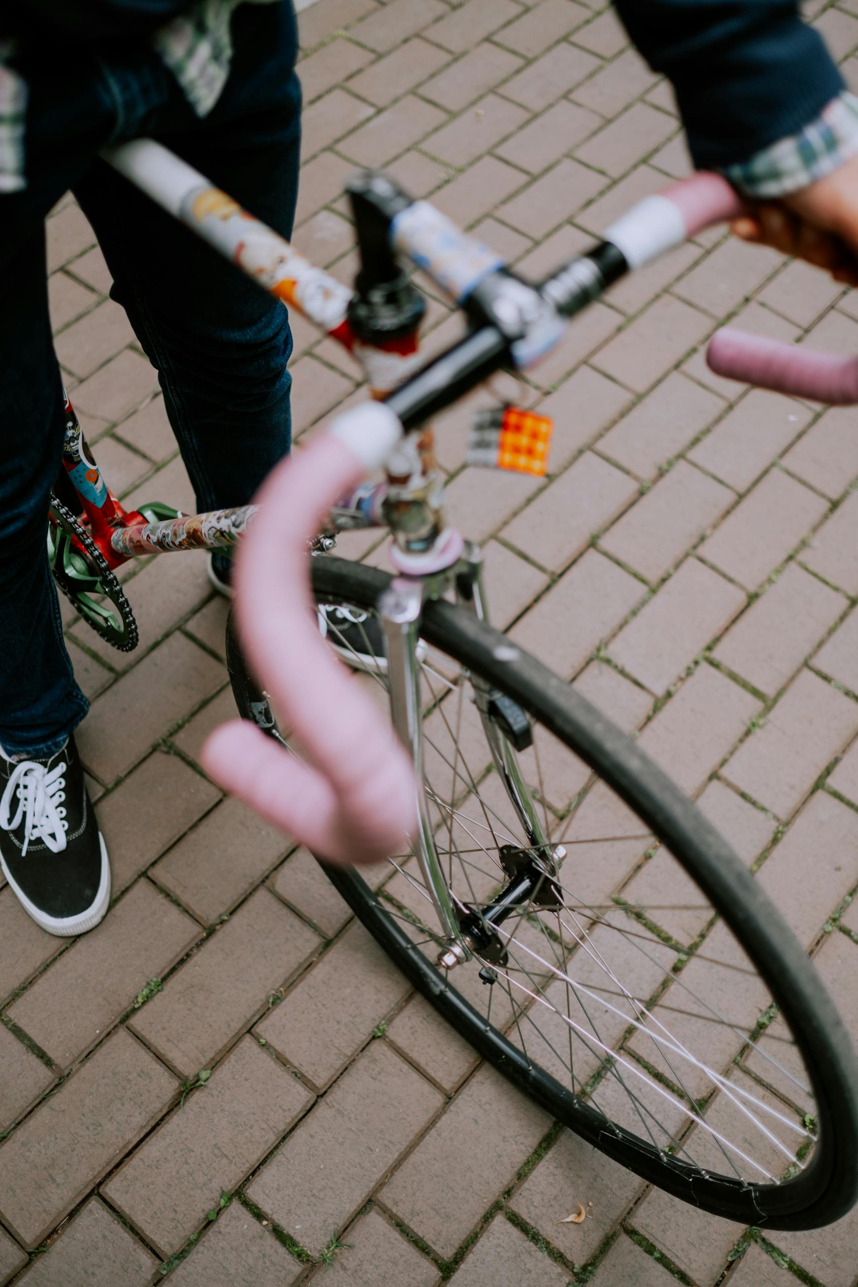 Close-up of a person riding a colorful fixed gear bicycle on brick pavement, emphasizing urban cycling lifestyle.
