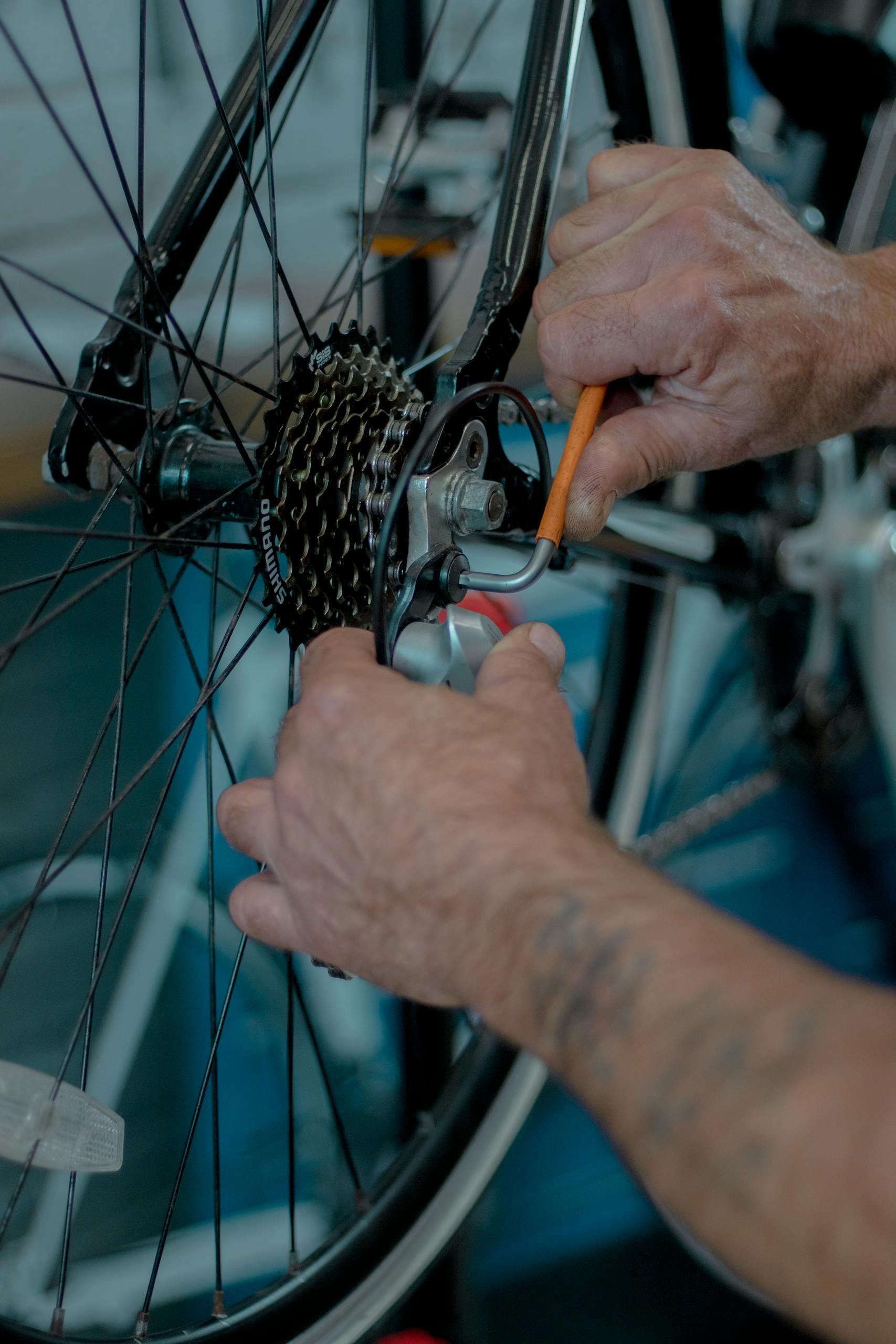 Hands working on bicycle gear in a workshop, showcasing repair tools.