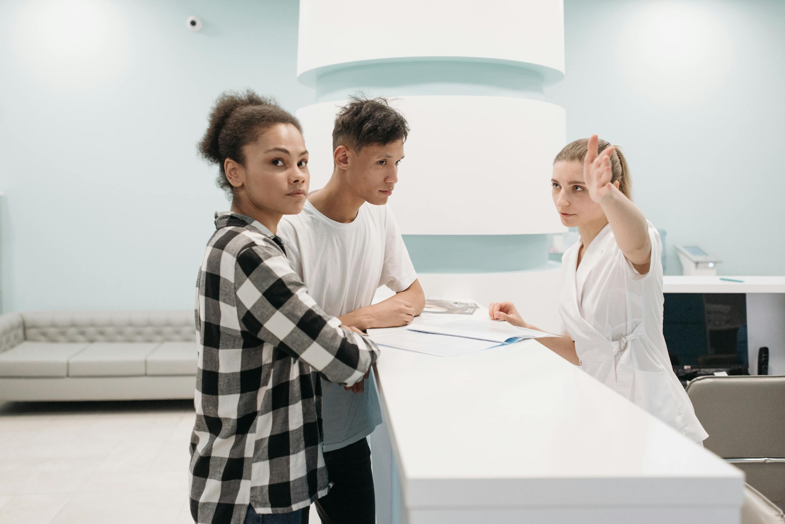 Two patients at hospital reception desk interacting with receptionist in white attire.