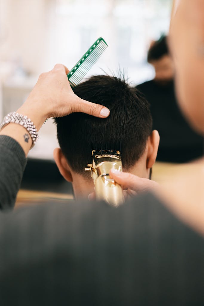 Back view of a man receiving a professional haircut with a comb and clipper.
