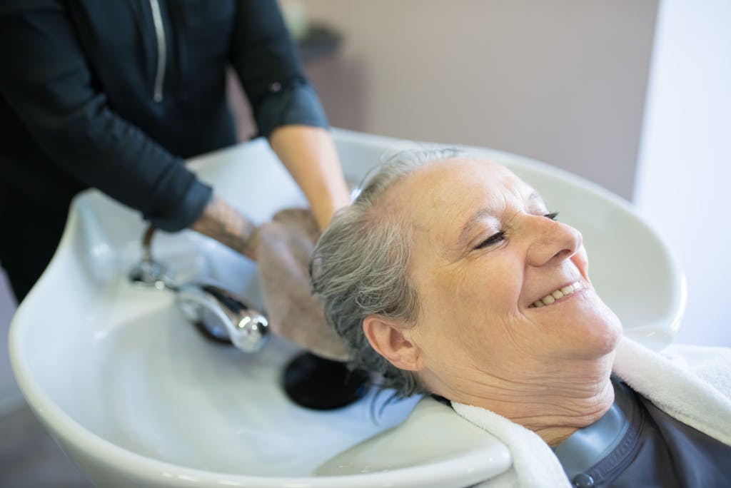 Senior woman smiling while getting her hair washed at a salon sink by a hairdresser.