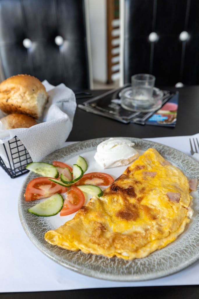 Tasty omelet served with fresh salad and bread rolls in a cozy cafe setting.